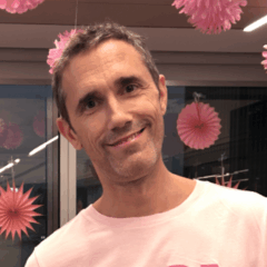Matt Bower smiling, wearing a pink shirt and surrounded by pink decorations.
